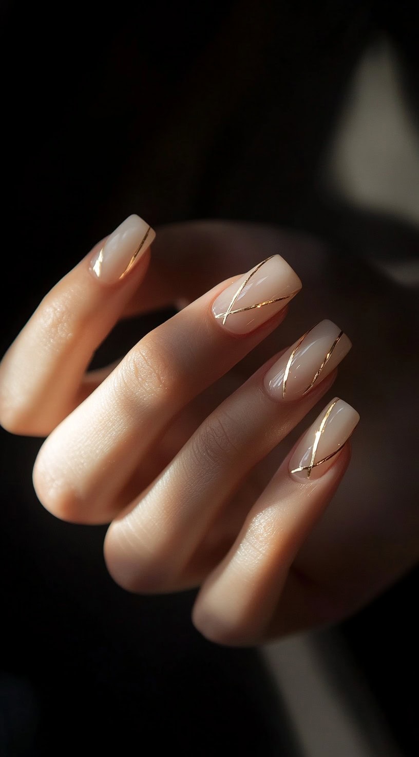 Short, square-shaped nails with a soft nude base and fine gold diagonal lines for an ultra-minimalist, chic aesthetic.