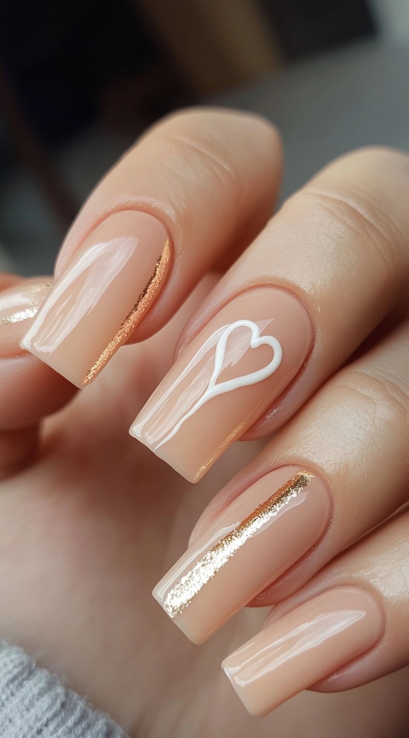 Nude coffin nails featuring minimalist gold foil stripes and a white heart outline on the ring finger.