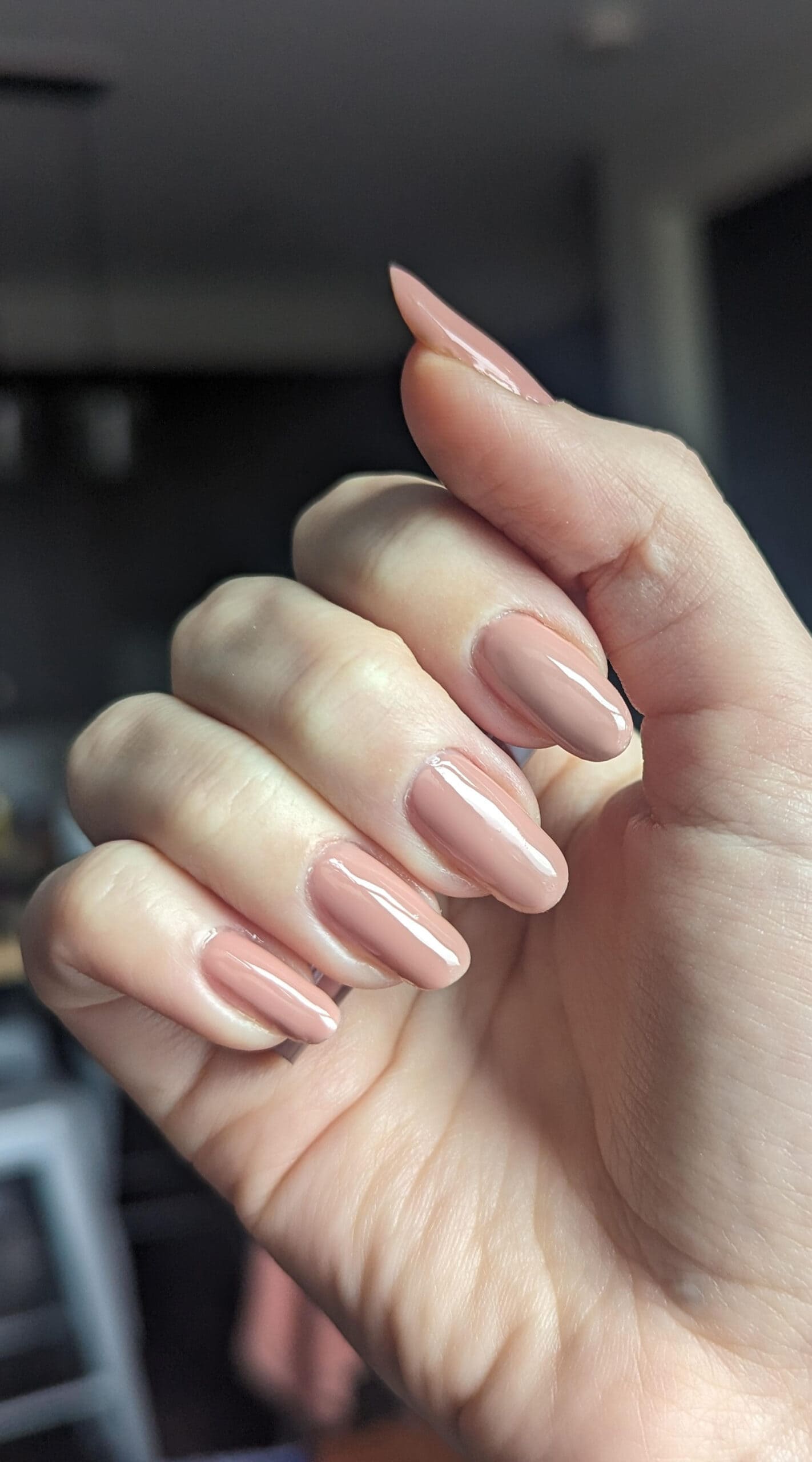 A hand showing freshly finished nude gel nails with a glossy, smooth finish under natural lighting.