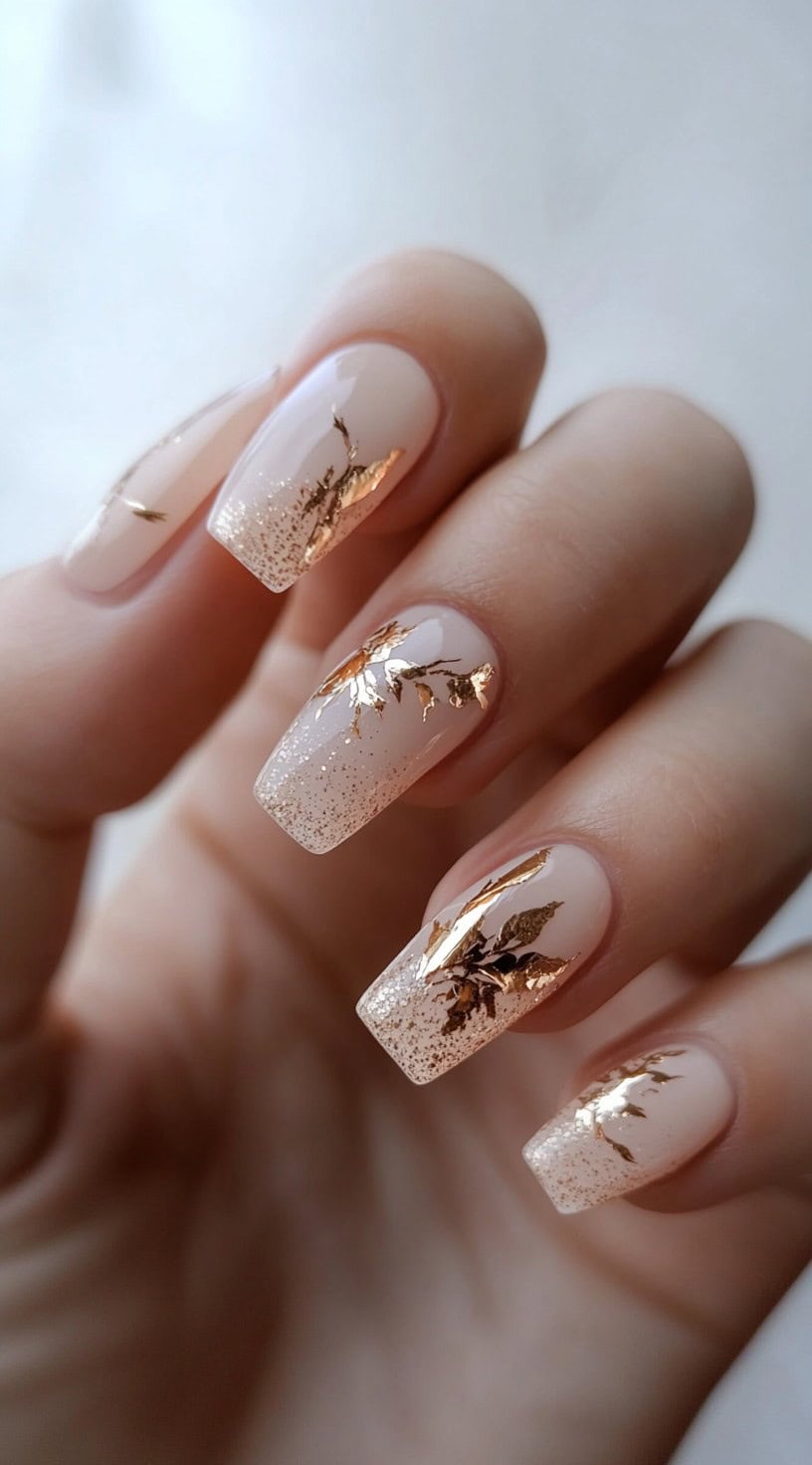 Square nails with nude base, gradient glitter tips, and gold foil floral detailing.