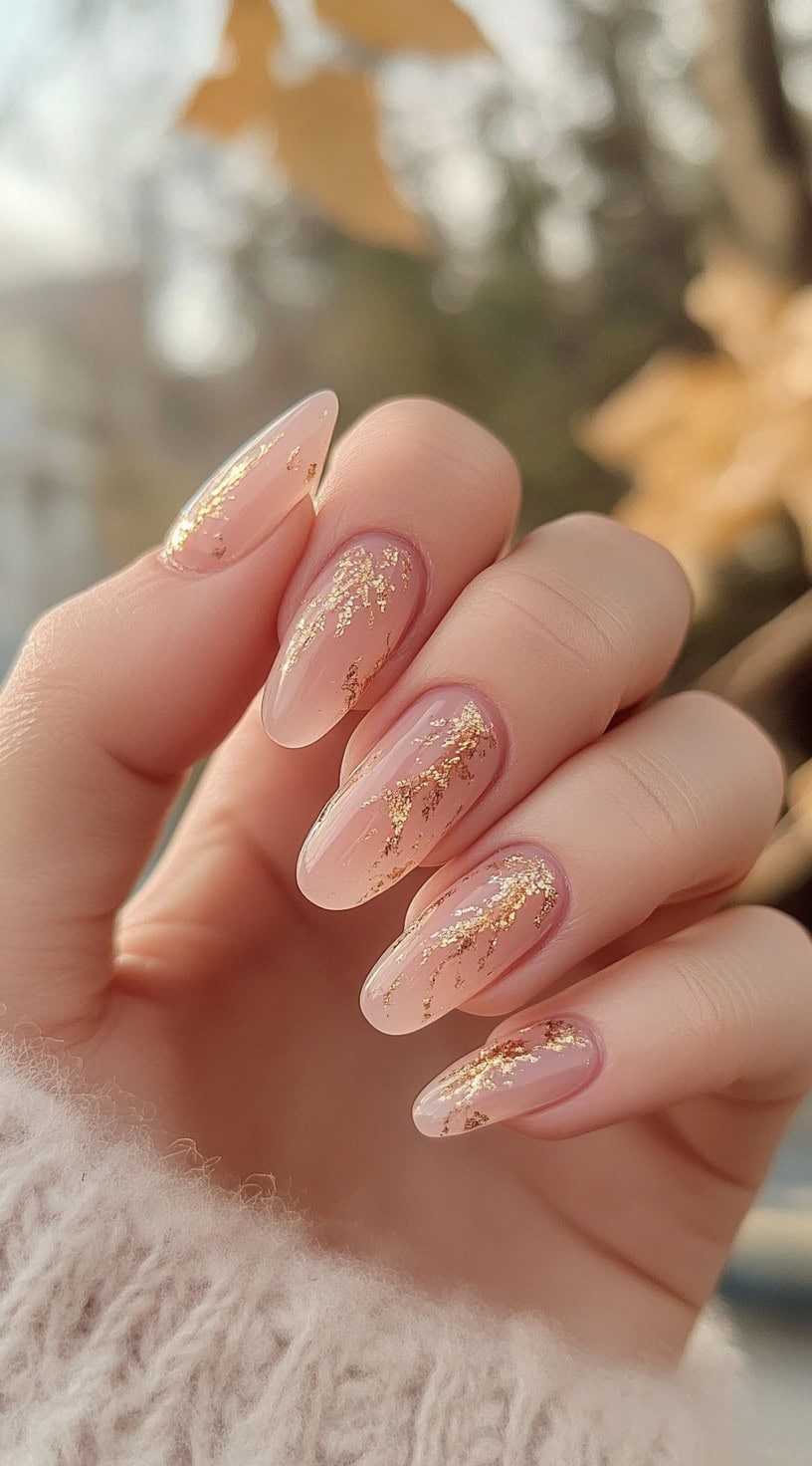 A set of almond-shaped nude pink nails with delicate gold foil accents for a touch of luxury.