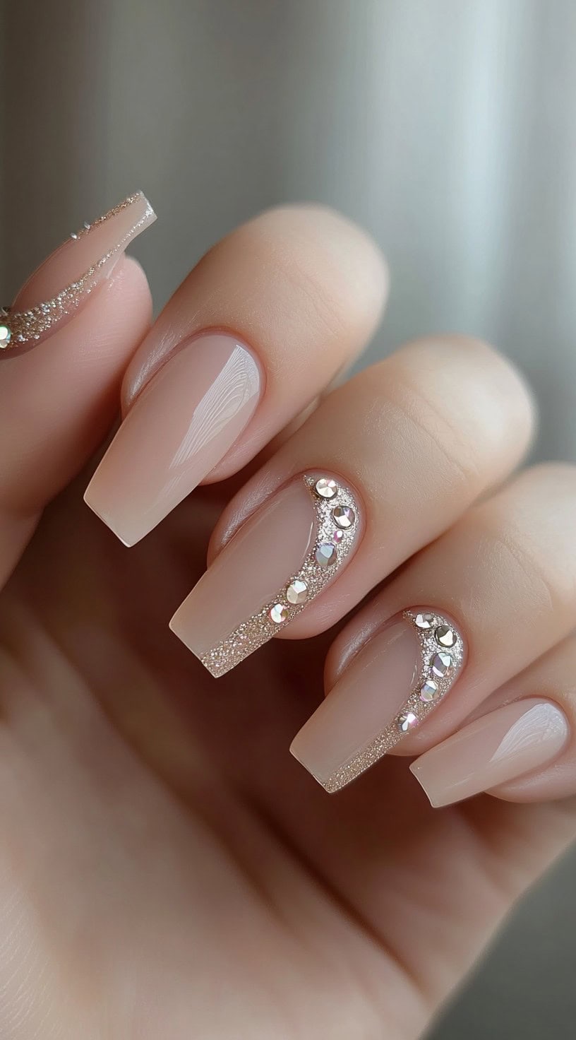 A set of nude-colored square-shaped wedding nails with delicate glitter wave designs and crystal embellishments along the curves.