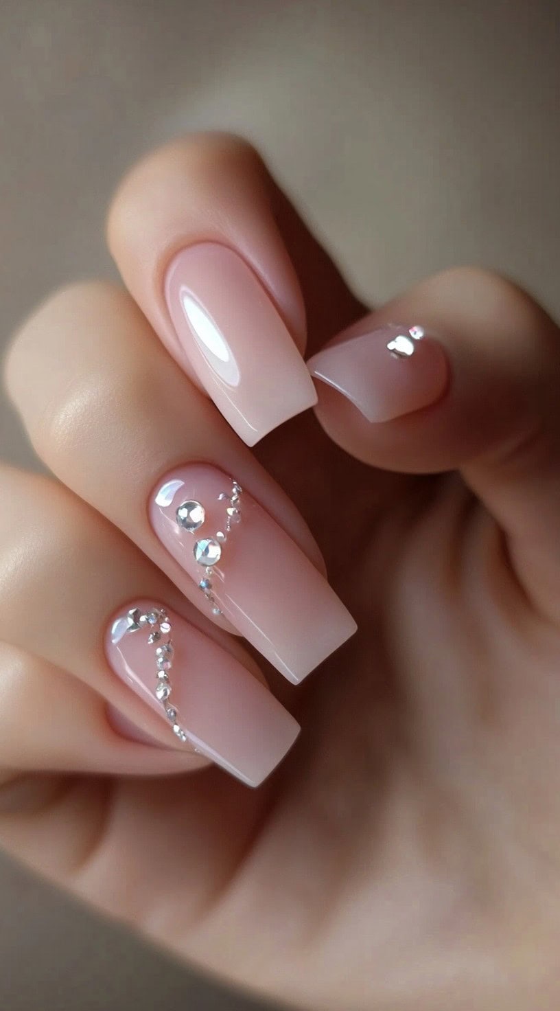 Neutral-toned square nails with rhinestone accents arranged in elegant patterns on two fingers.