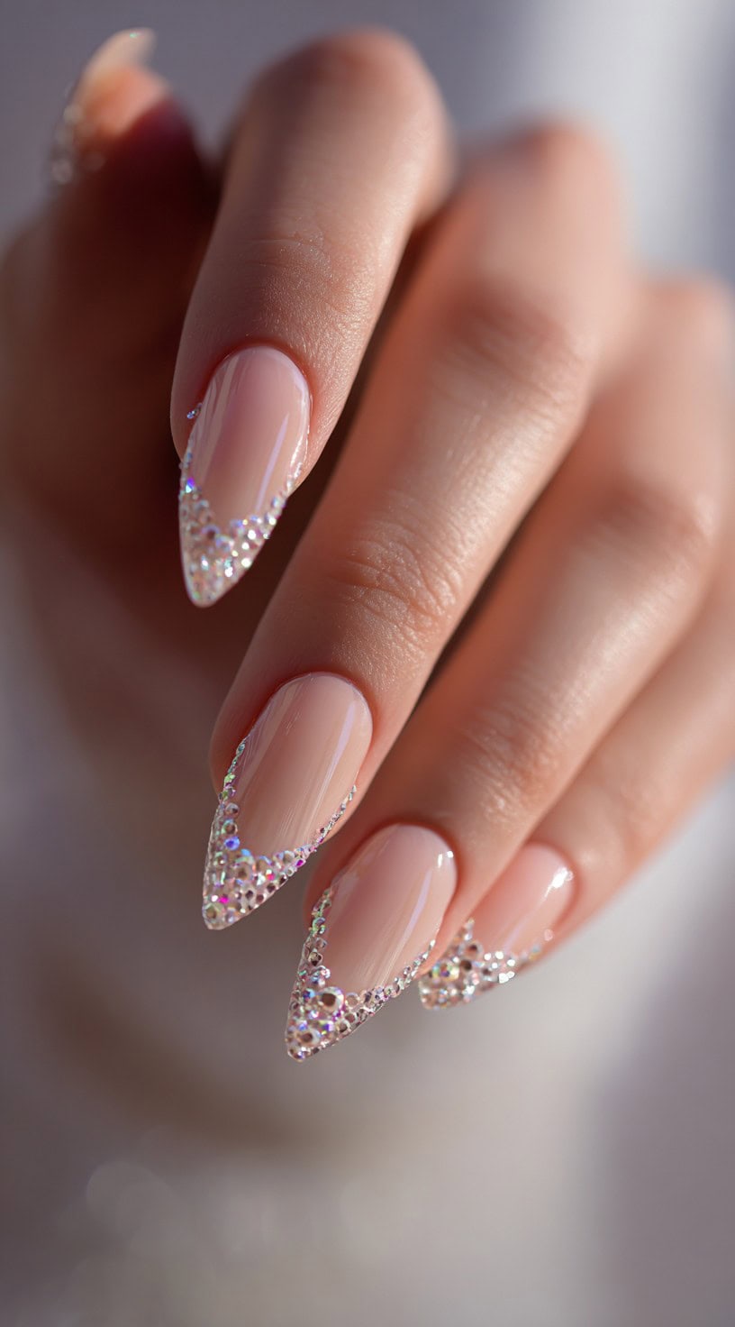 Stiletto-shaped nude nails with pointed tips fully outlined in glistening, multi-sized rhinestones.