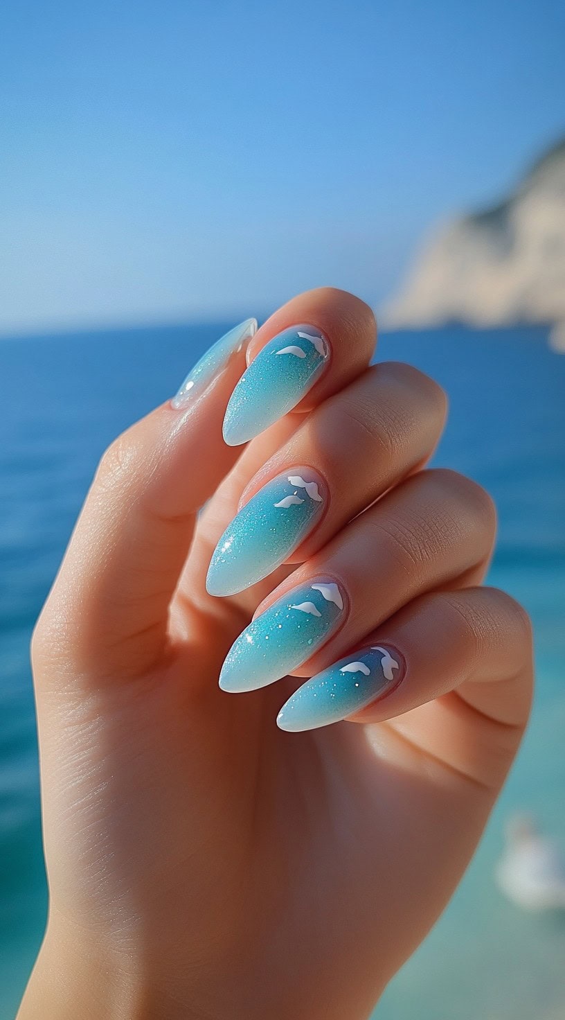 Almond-shaped nails with blue gradient and white wave accents.