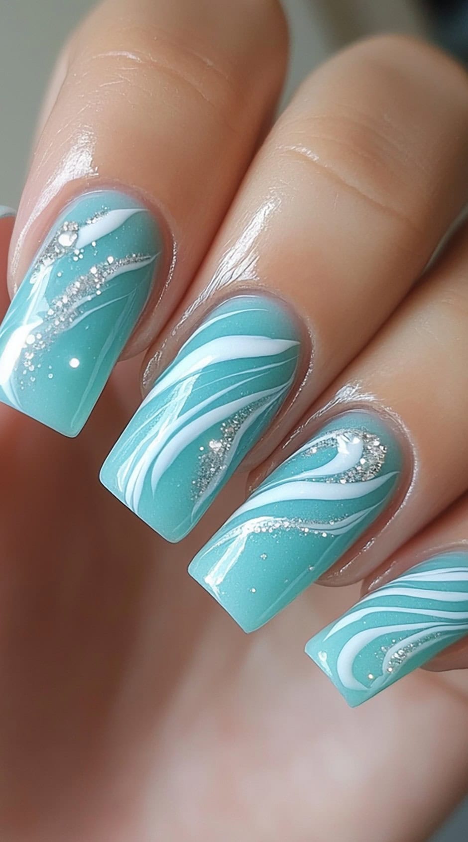 Glossy square-shaped nails with aqua blue base, white wave-like swirls, and fine silver glitter accents.