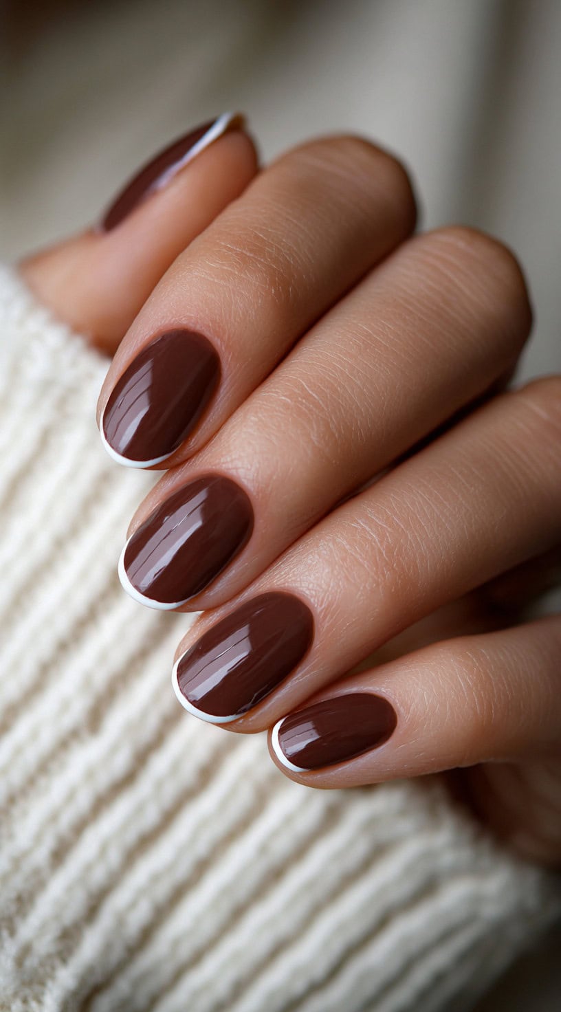 Oval-shaped nails painted in chocolate brown with ultra-thin white French tips along the edges.