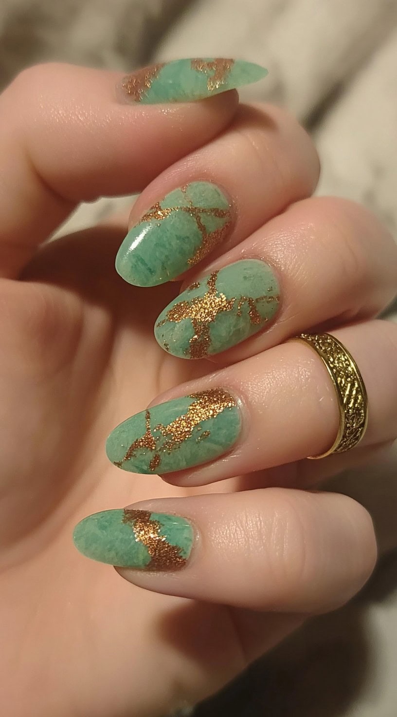 A hand with medium-length oval nails painted in a soft jade tone with fine coppery-gold vein detailing inspired by kintsugi.
