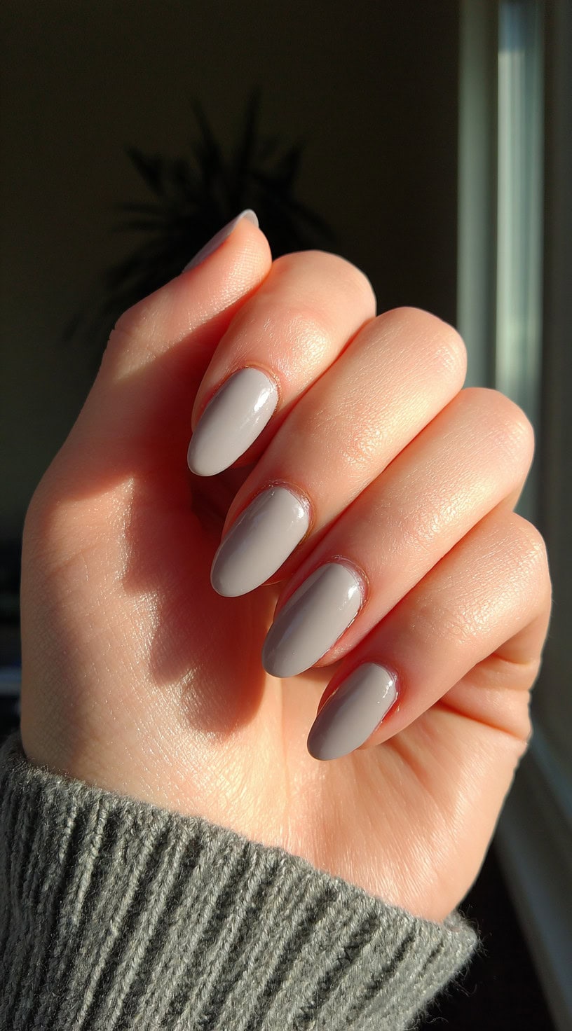 Oval-shaped nails painted in a warm taupe-gray color with a glossy finish.