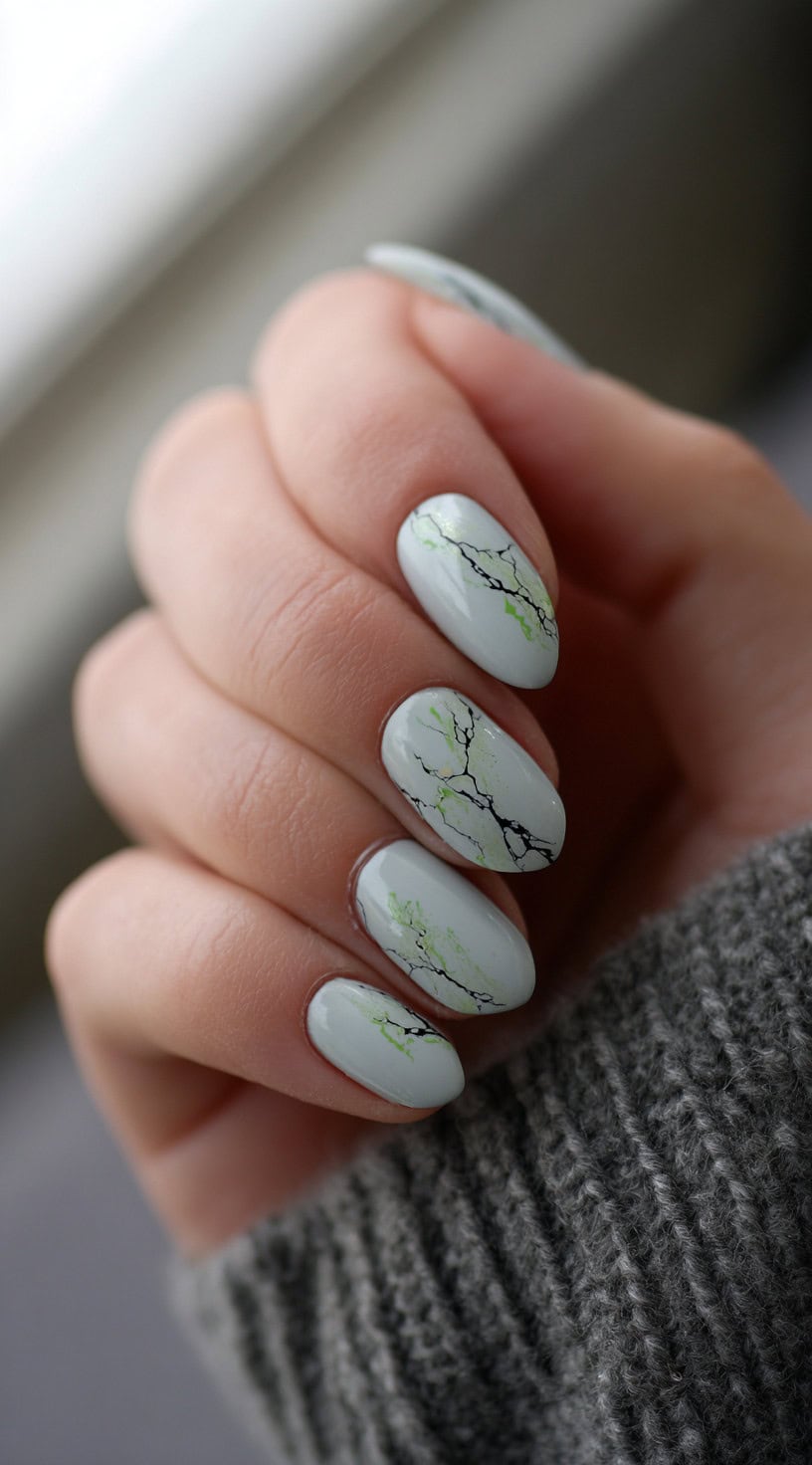 Almond-shaped nails painted in soft green with faint black and lime-green veining resembling slow skin rot.