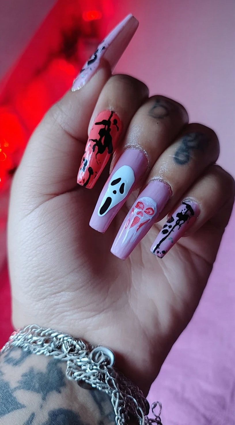 Coffin-shaped nails painted in pastel pink with ghostly faces, black and red splatters, and dripping accents.