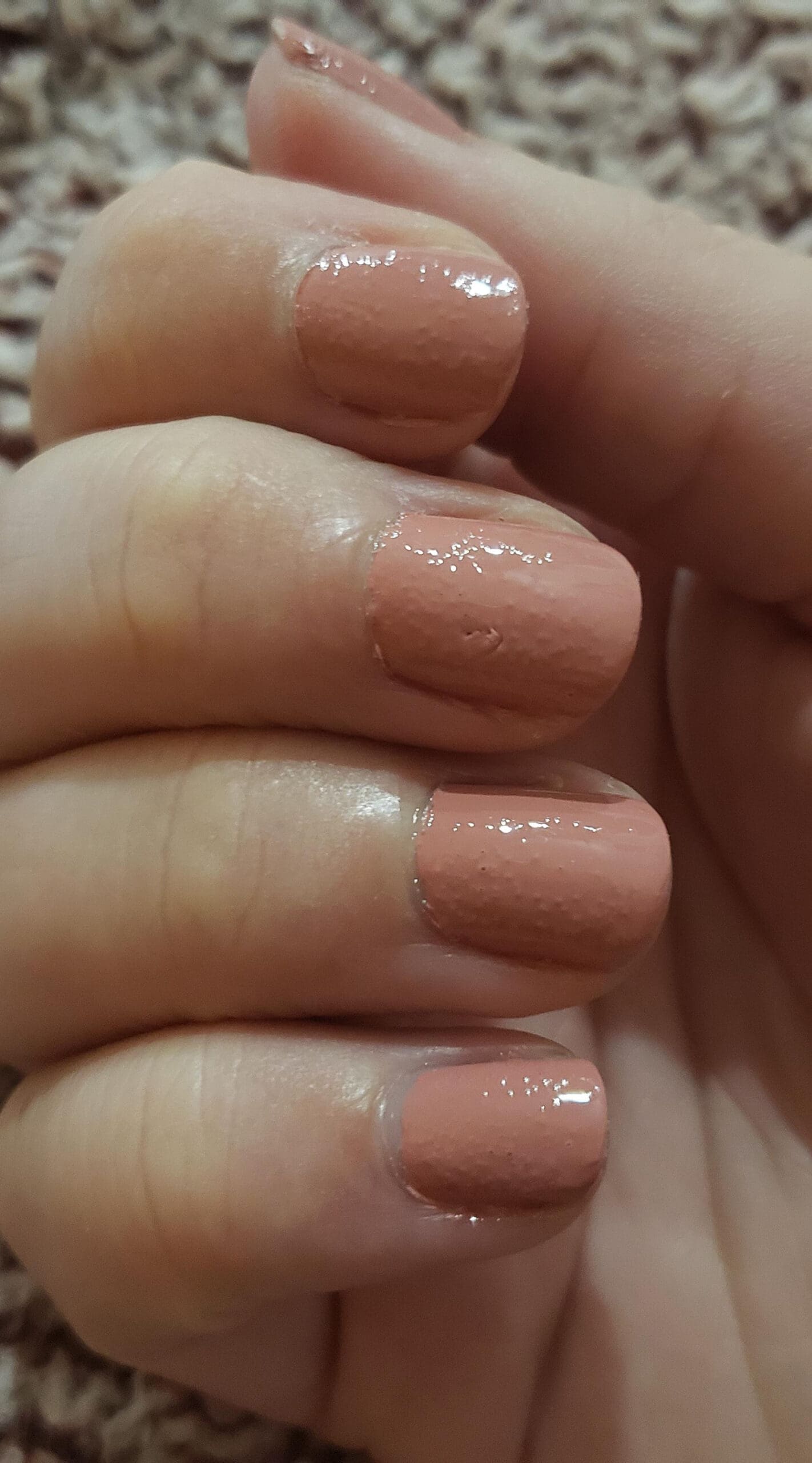 Manicure featuring peach-toned polish with clear bubbling and a patchy, bumpy finish under glossy top coat.