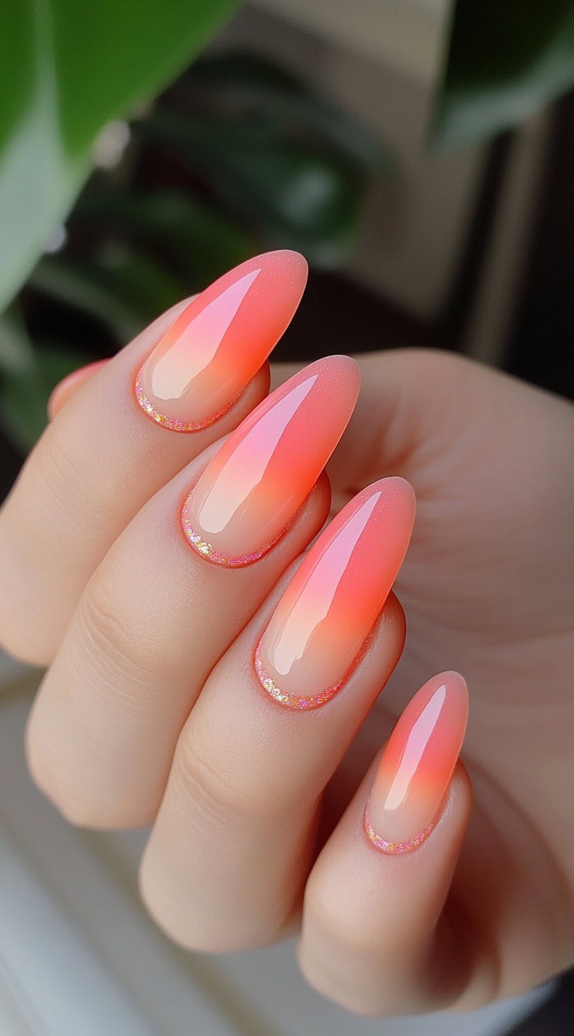 Short almond-shaped nails with a soft pink-to-peach gradient and a thin, glittery pink outline near the cuticle.