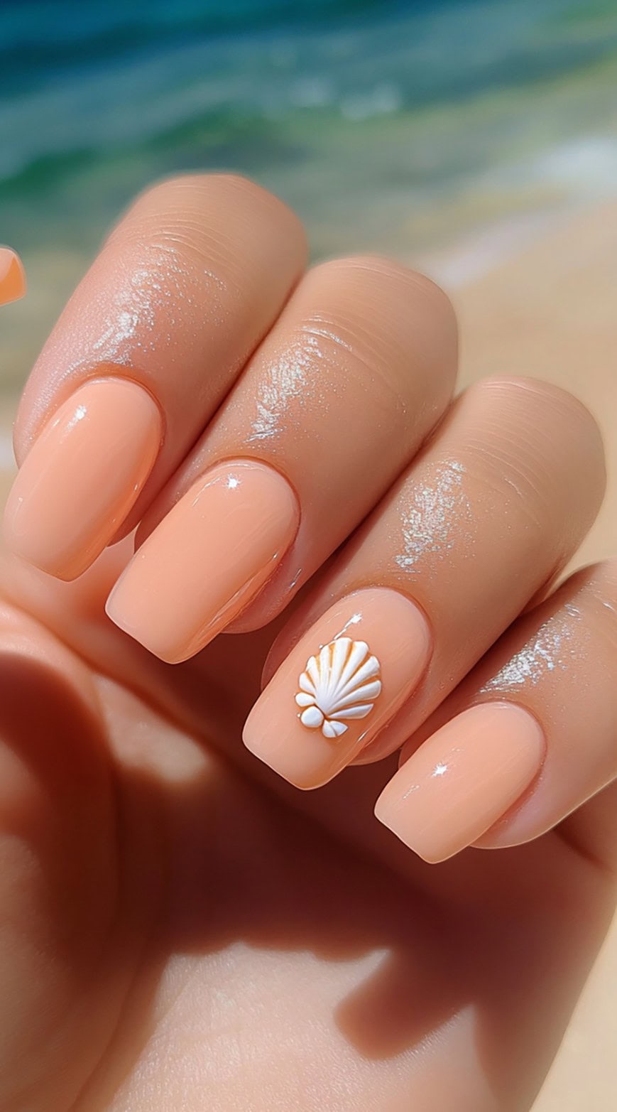Hand with square-shaped peach nails featuring a white shell accent on one nail.