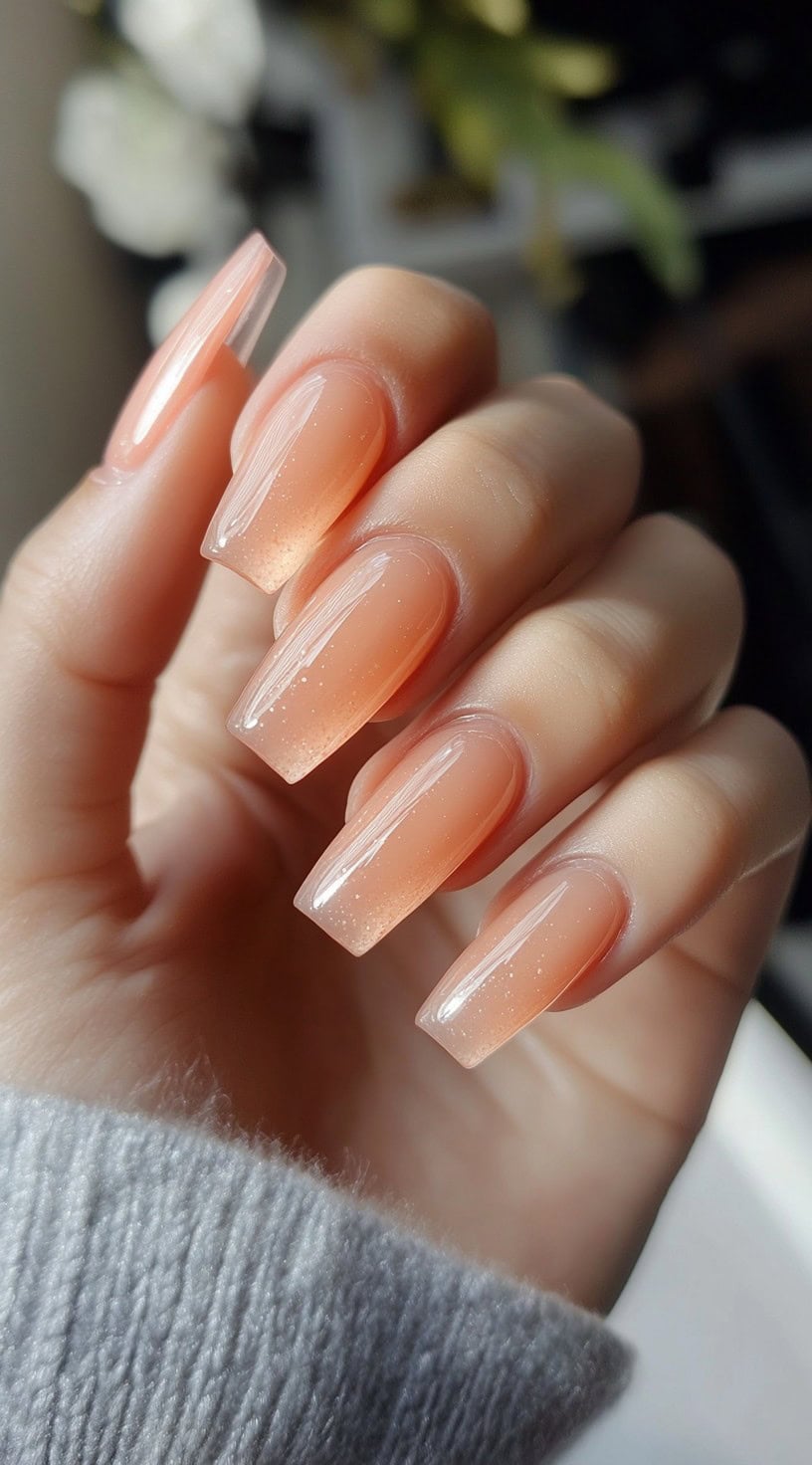 Coffin-shaped nails with a warm peachy hue and fine shimmer for a soft, glowing effect.