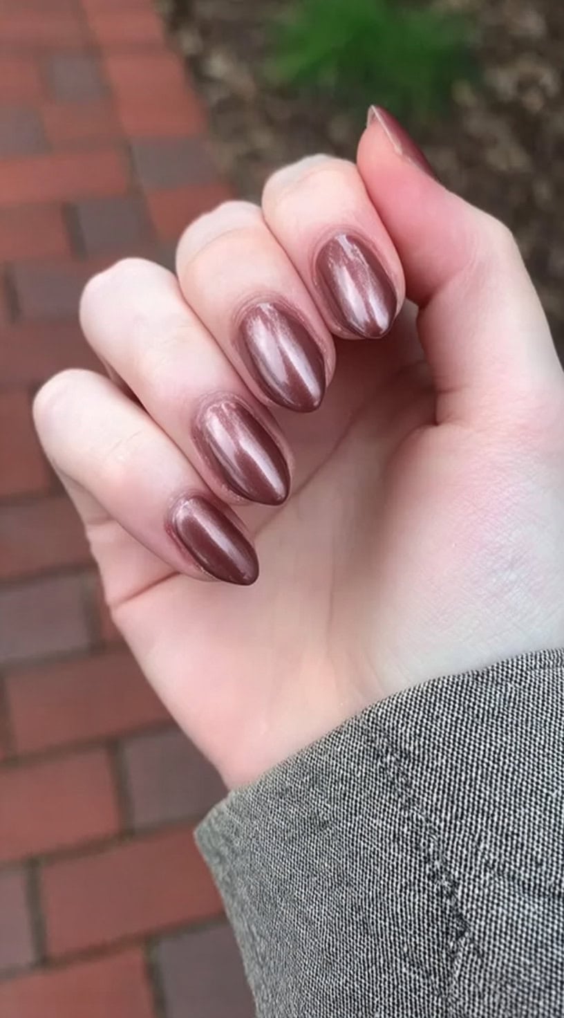 Almond-shaped nails in a pearlized mocha tone, shimmering under natural daylight on pale skin.