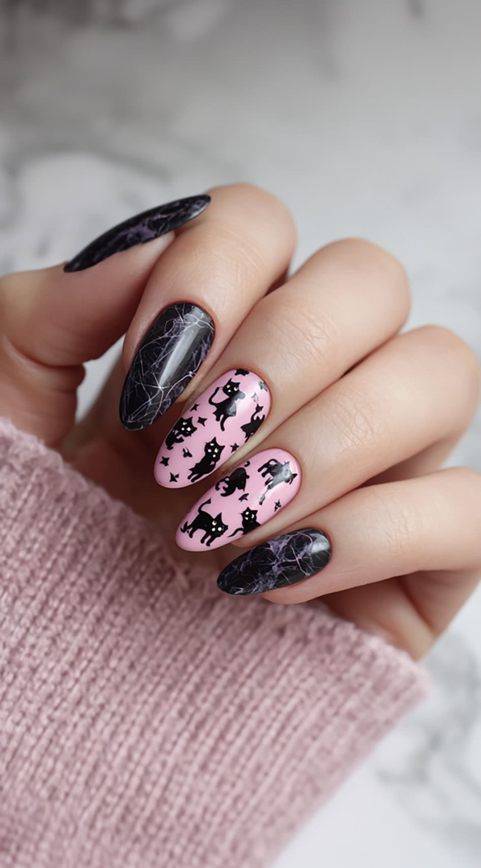 Almond-shaped nails alternating between pink and black, with the pink ones covered in scattered black cats and stars, and the black ones decorated with white web lines.