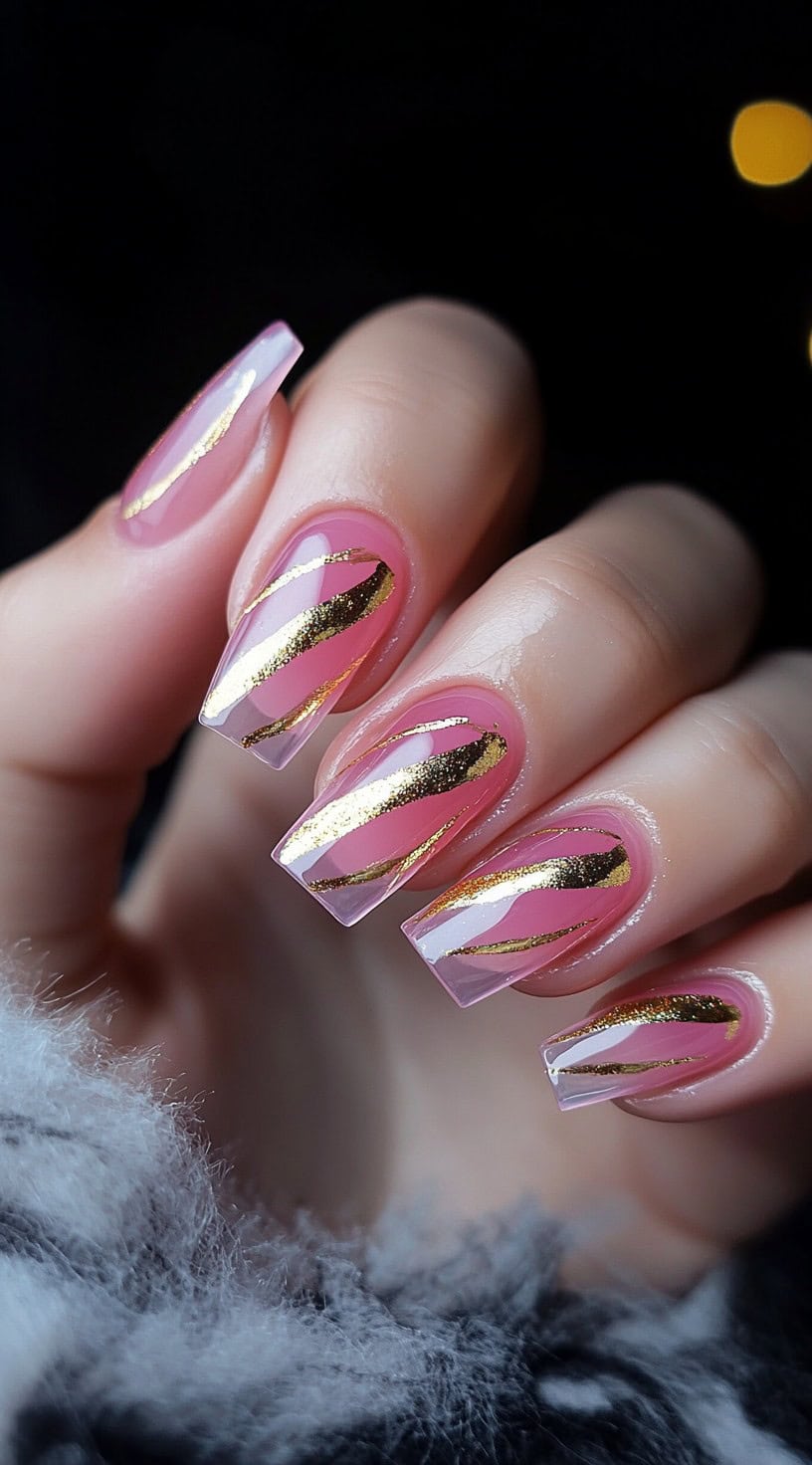 A close-up of square-shaped nails with a sheer pink base, decorated with elegant gold swirls in a fluid, artistic design.