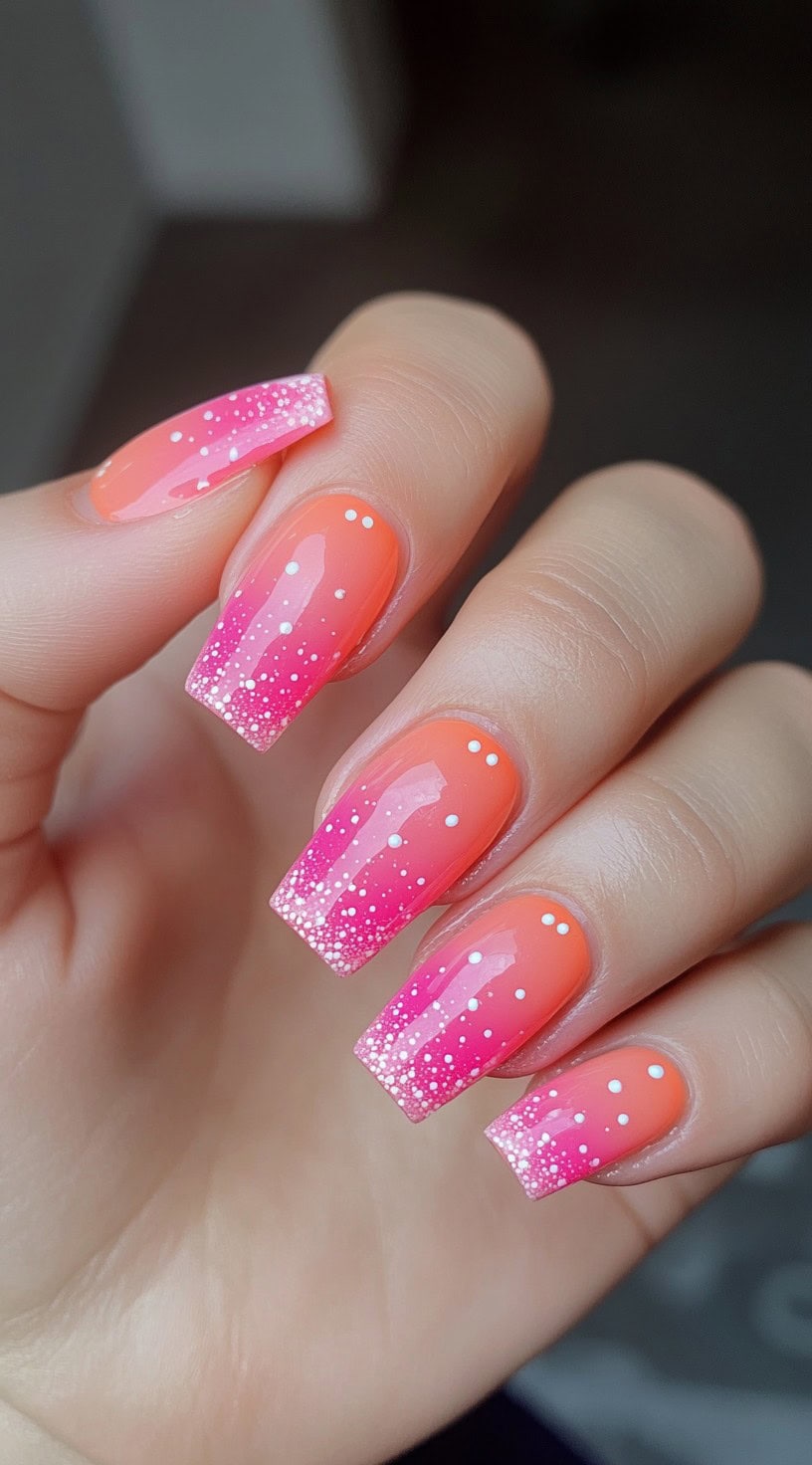 Square nails with a gradient fade from orange to pink, finished with white glitter dots and speckled tips.