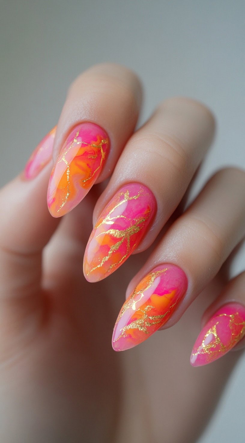 Almond-shaped nails featuring a marbled blend of pink and orange with scattered gold foil accents.