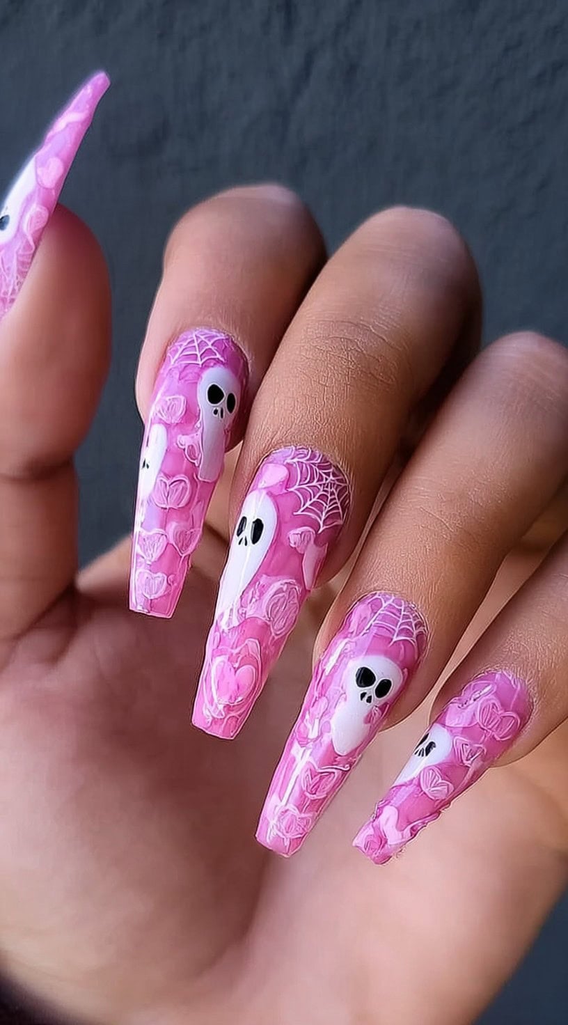 Hand with long pink coffin nails decorated with white ghosts, black eyes, and white spiderweb details.