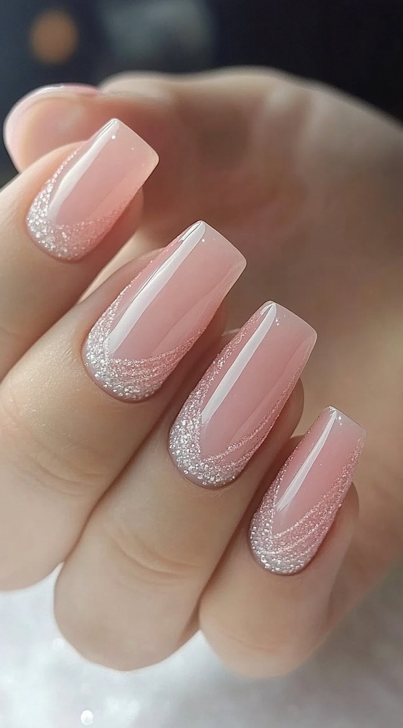 Square nails with a clear pink base and sparkling glitter swirls along the tips in a curved French pattern.