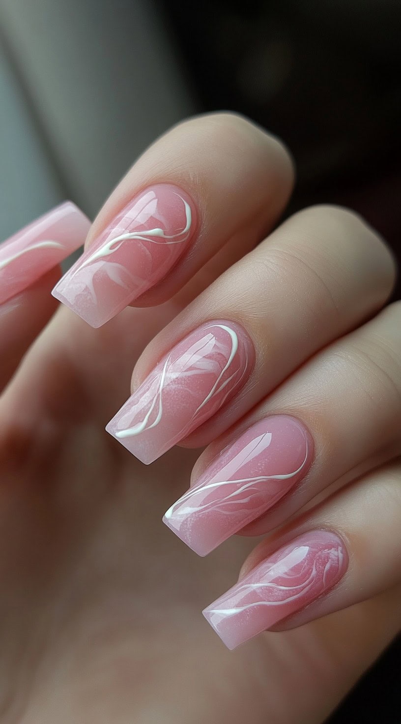 A set of long, coffin-shaped nails in a soft pink shade, featuring delicate white swirls resembling marble patterns.