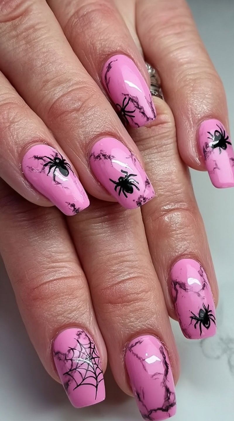 Hand with short pink nails decorated with black marble patterns, spiders, and a spiderweb design.