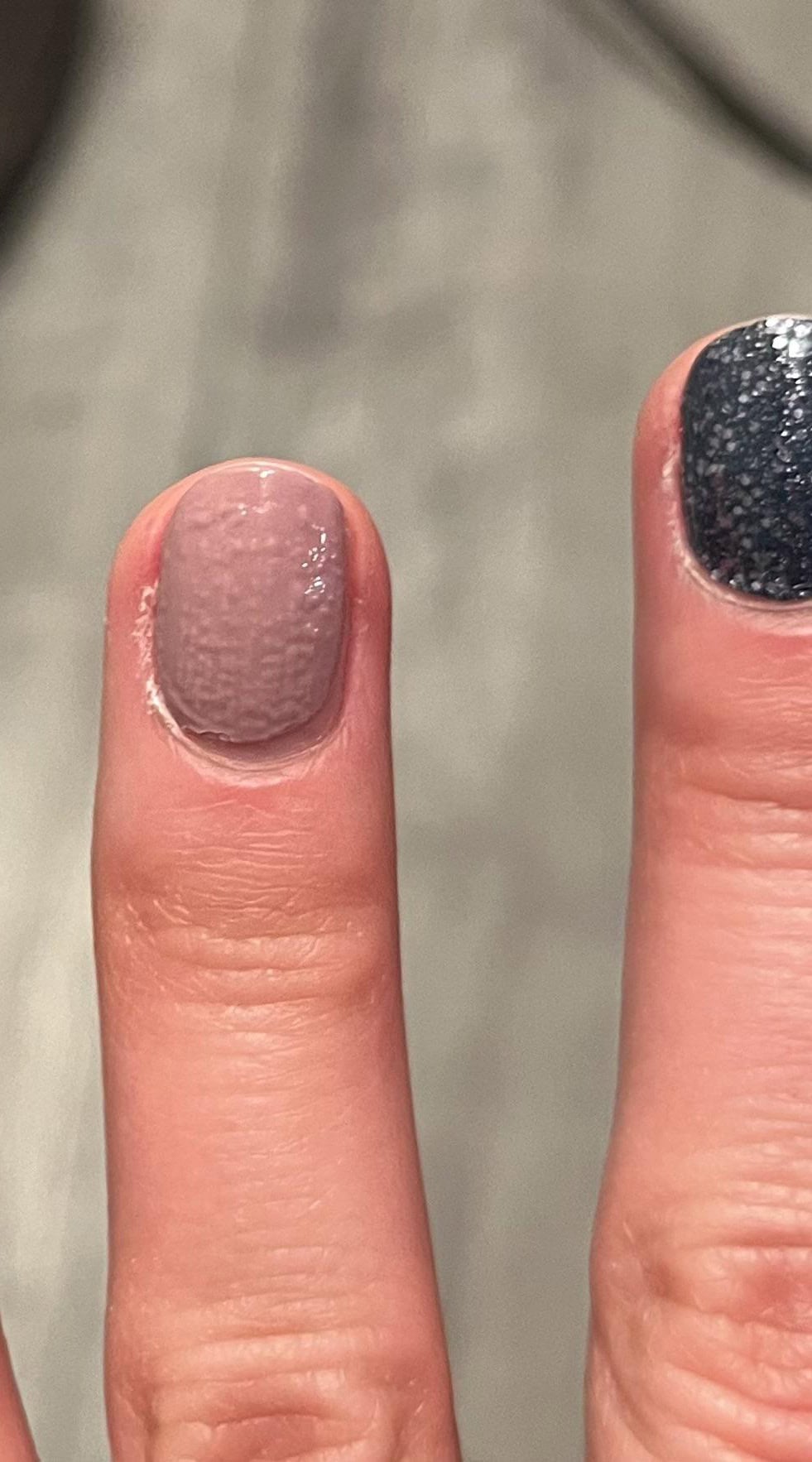 Close-up of a fingernail painted with pale pink nail polish showing heavy bubbling and a textured, uneven surface.