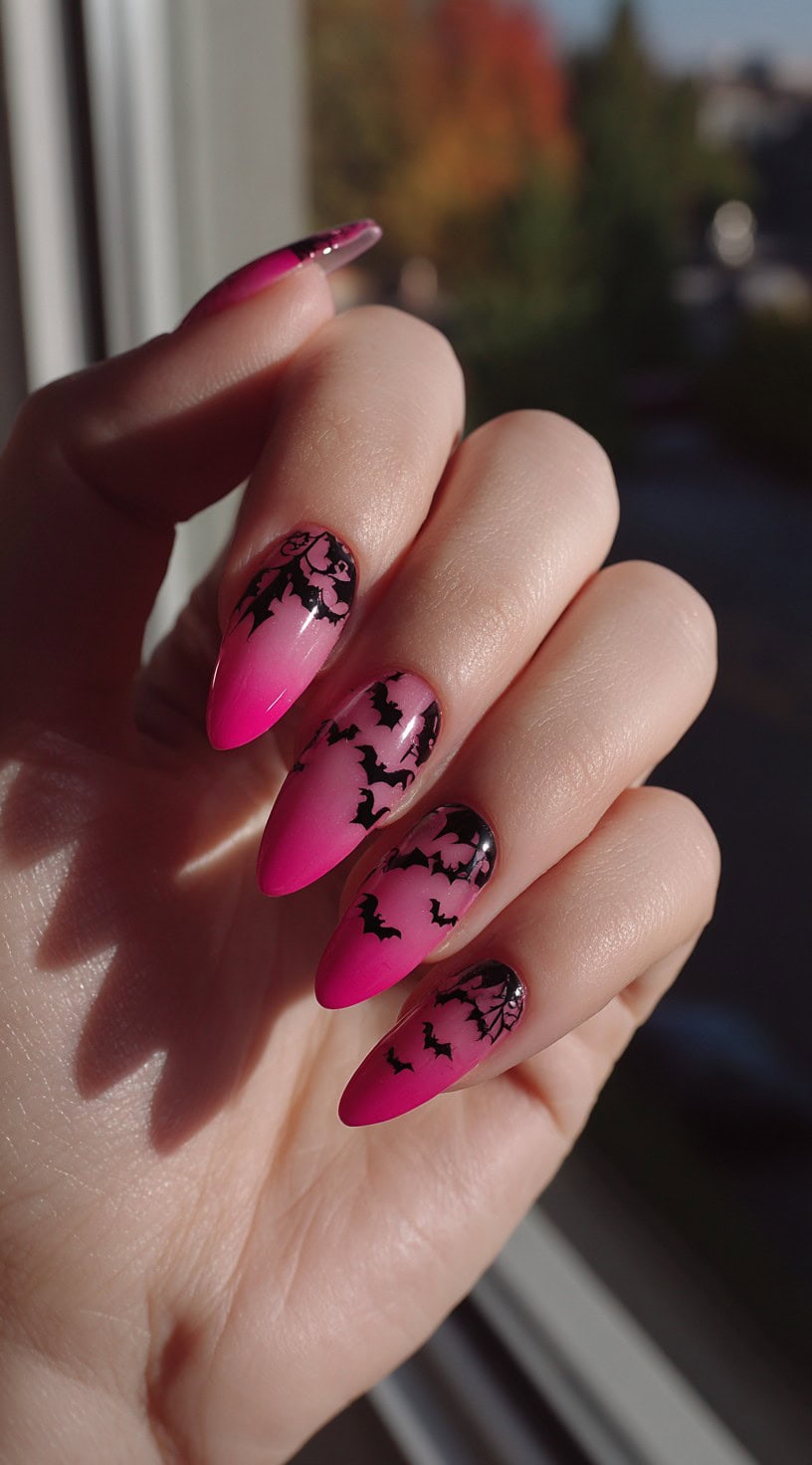Hand with almond-shaped nails in a pink ombre with black bat silhouettes and spiderweb details.