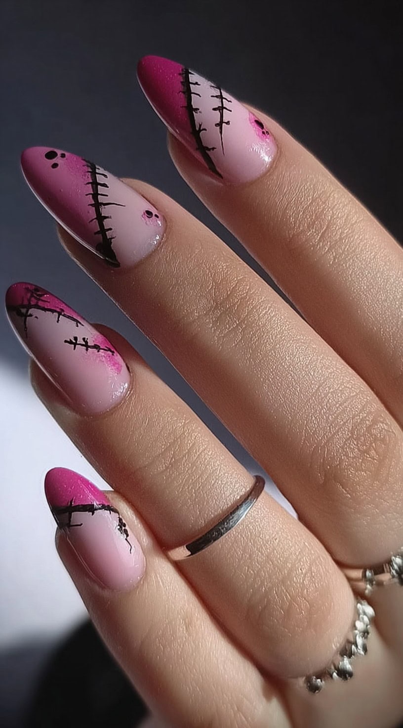 Hand with almond pink ombre nails featuring black Frankenstein-style stitch details crossing each nail.