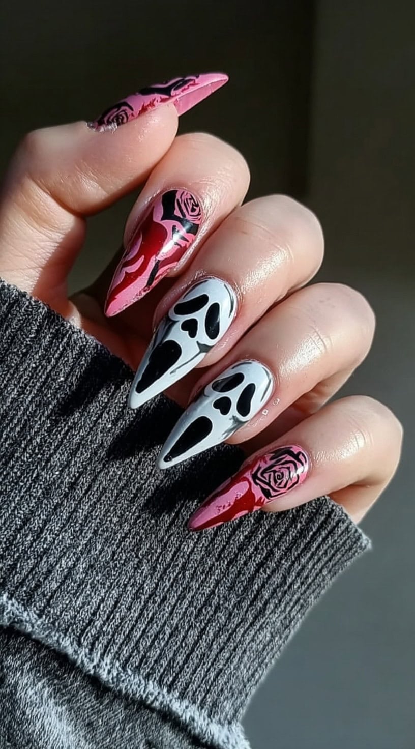 Hand with long stiletto nails decorated with pink and black roses, red accents, and two nails featuring large white ghostface masks.