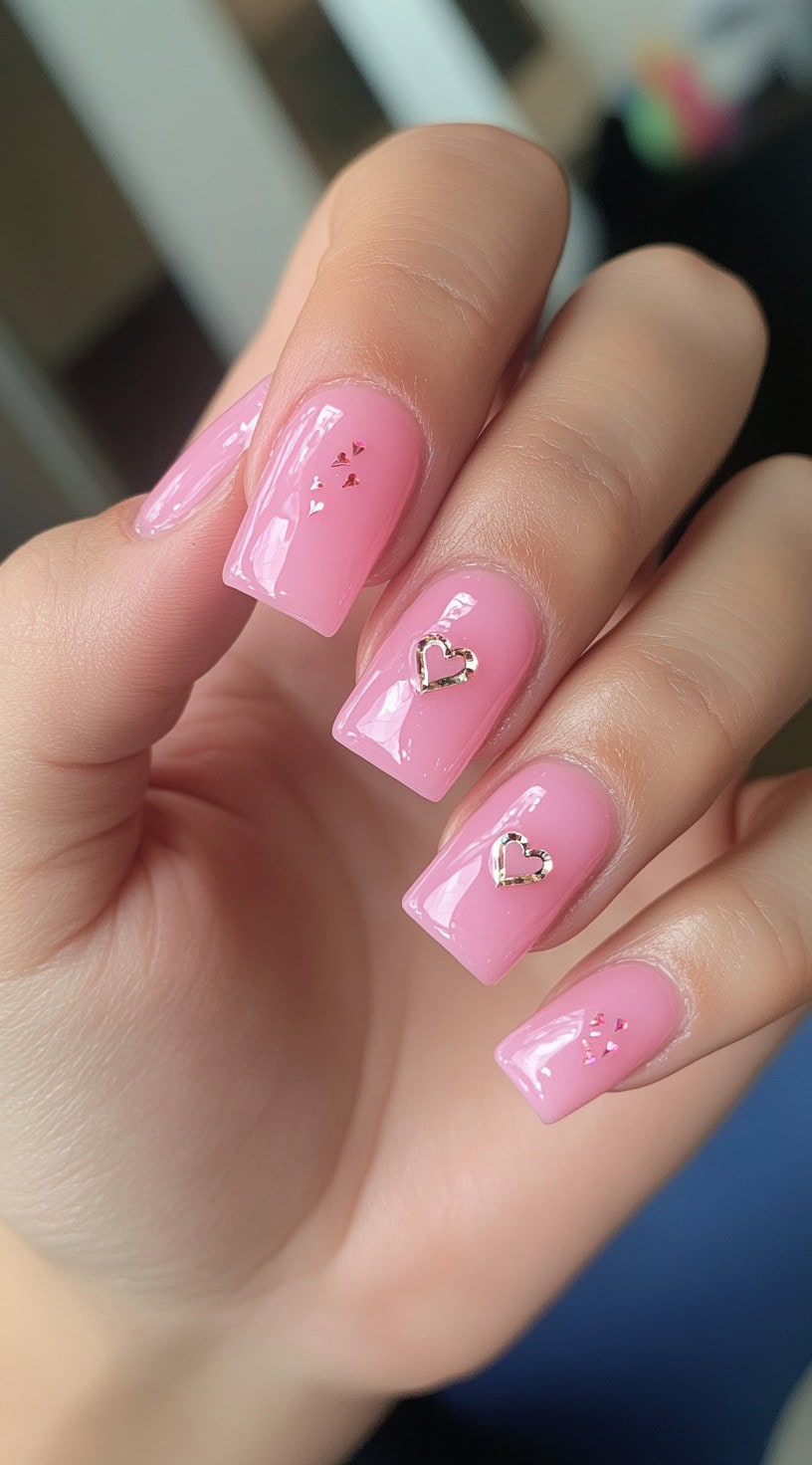 Bright pink square nails with small metallic heart accents placed delicately on two fingers.