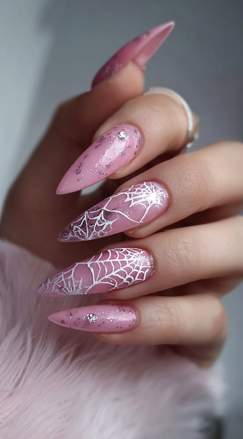 Hand with long pink stiletto nails decorated with silver glitter and white spiderweb designs.