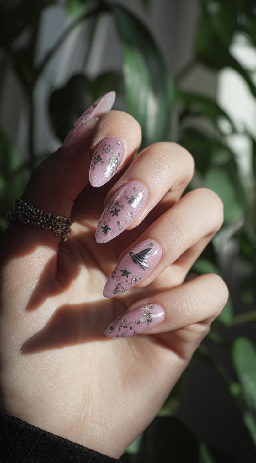 Hand with almond-shaped pink nails decorated with silver foil stars and witch hat charms for a mystical vibe.