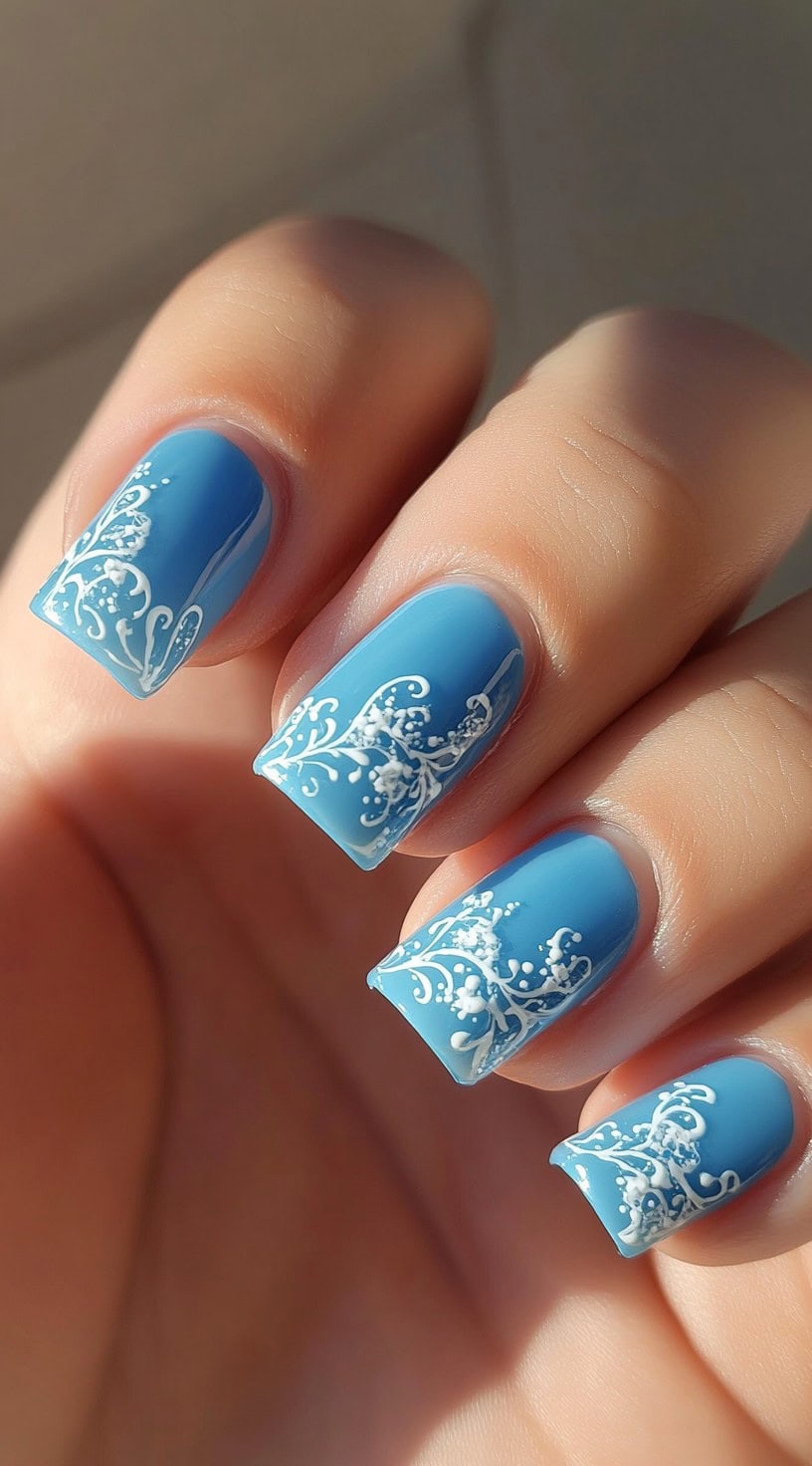 Soft powder blue square-shaped nails with intricate white lace-like detailing along the tips.