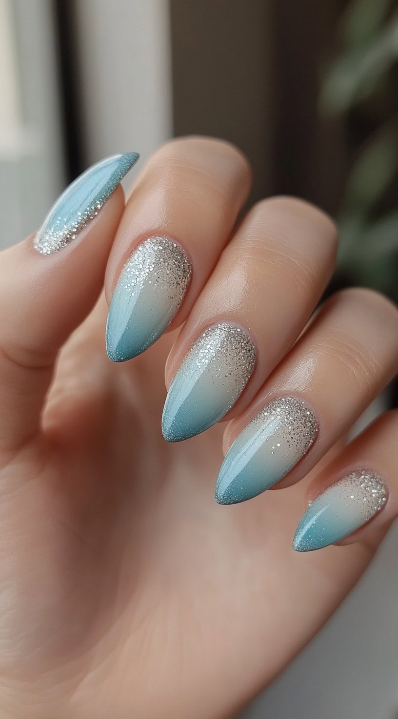 Almond-shaped nails with a powder blue to white ombre and fine silver glitter at the base.