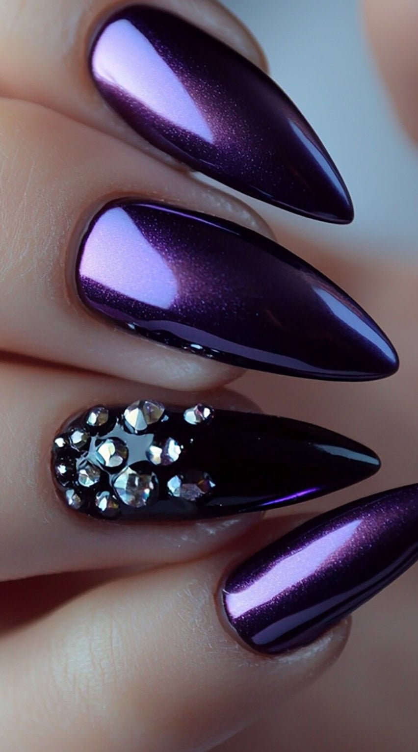 Glossy purple chrome stiletto nails with one accent nail adorned with crystal rhinestones.