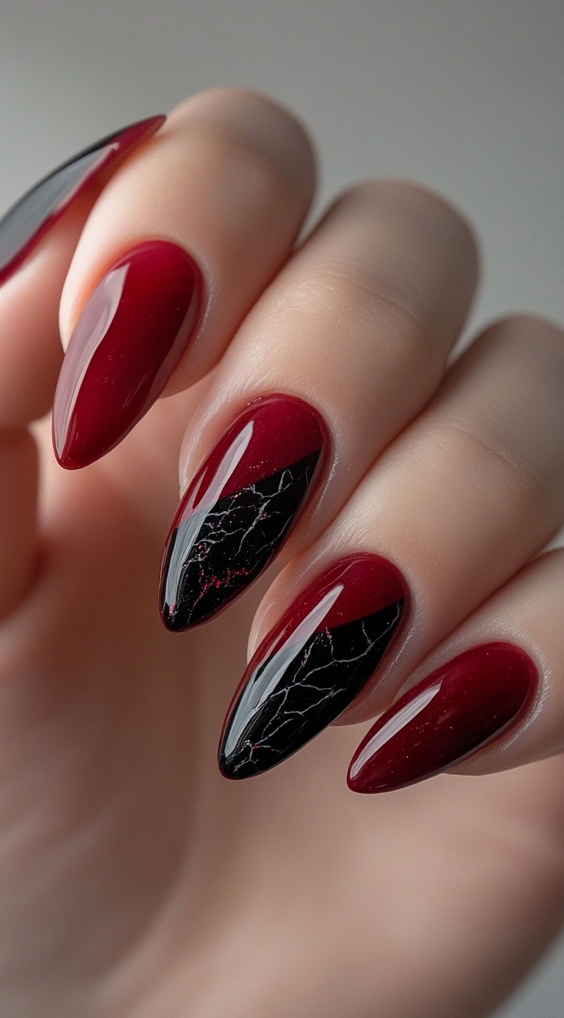 Almond-shaped nails in deep red, featuring black marble detailing on accent nails with fine white veining.