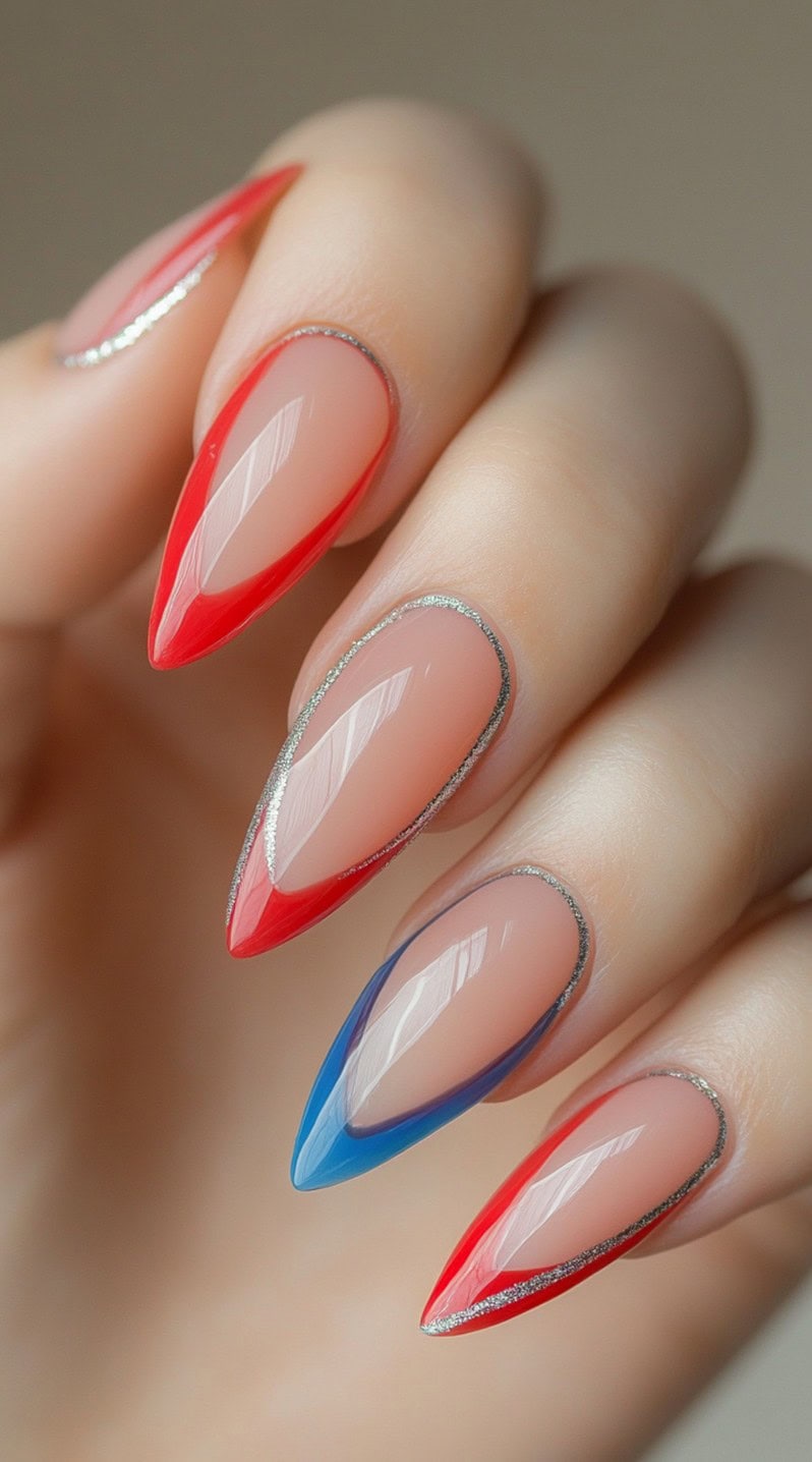 A hand featuring stiletto nails with a sheer nude base, outlined in alternating red and blue French tips with fine silver accents.