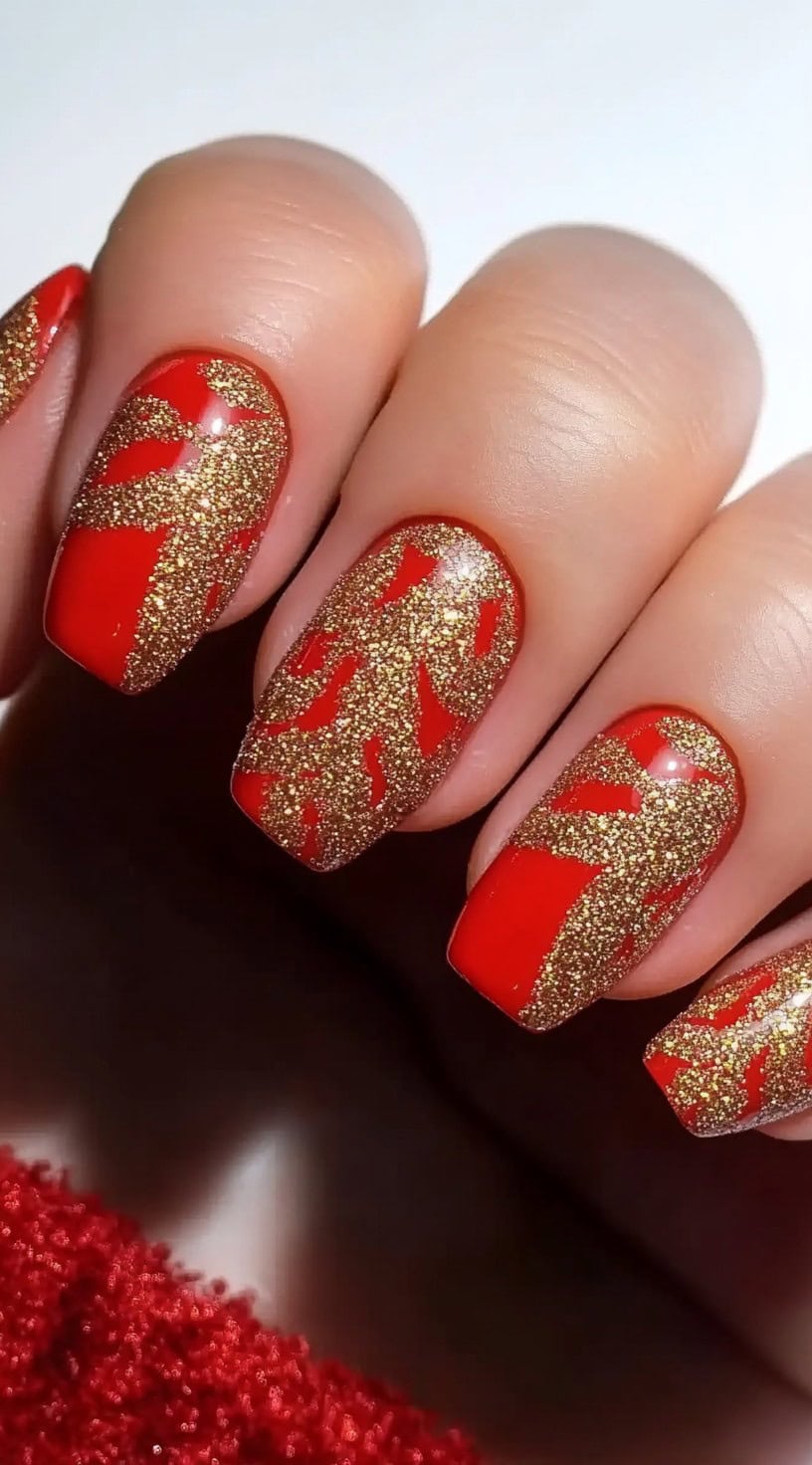 A vibrant red manicure with textured gold foil accents in an abstract design on square nails.