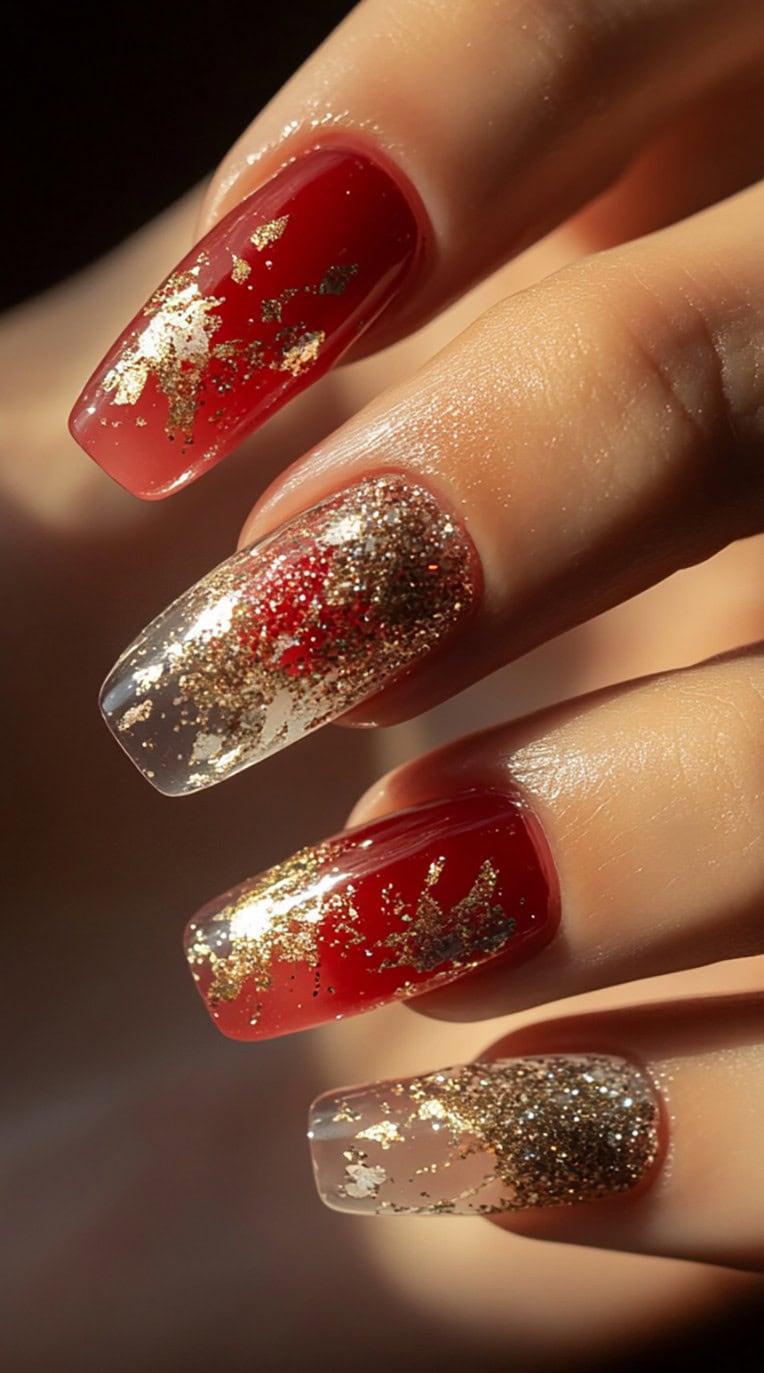 A set of square-shaped nails with a sheer-to-red ombre effect, accented with scattered gold foil for a luxurious finish.