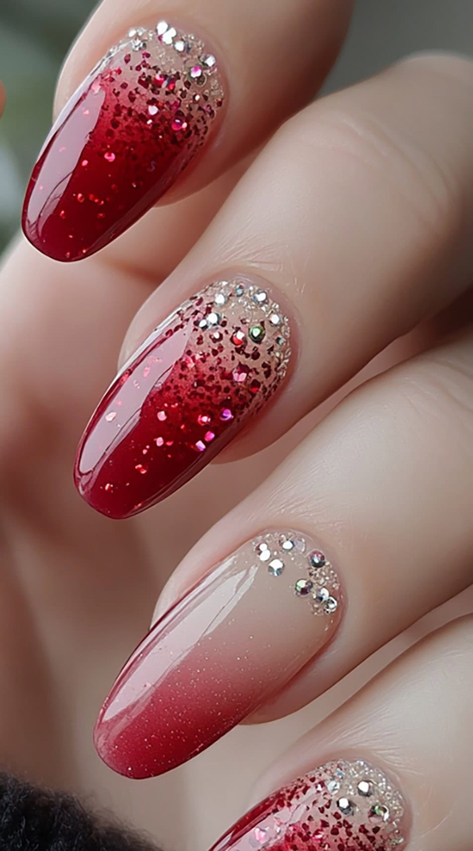 A stunning red-to-nude gradient manicure with scattered glitter and rhinestone accents on almond-shaped nails.