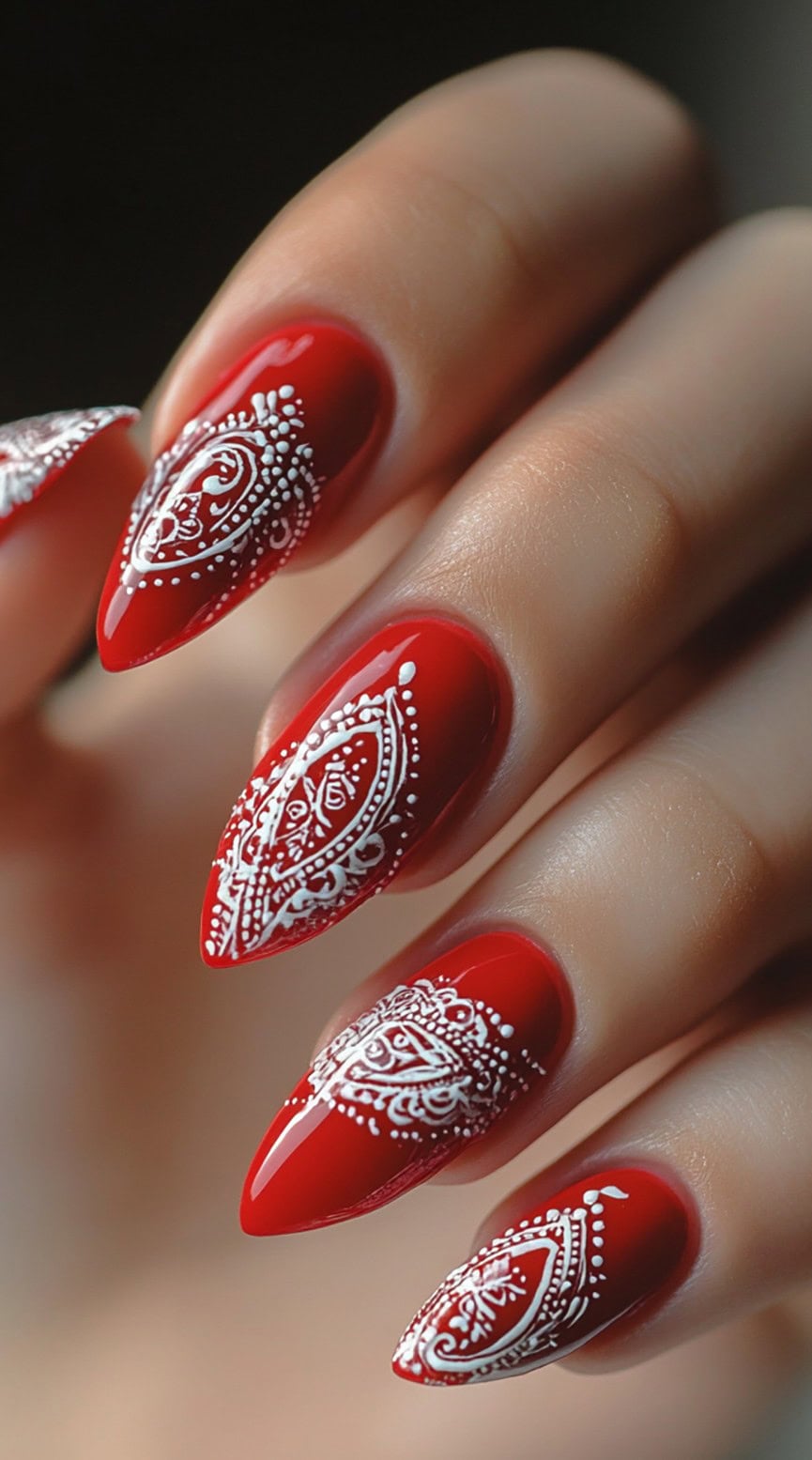 Sharp almond-shaped nails with a glossy red base featuring intricate white paisley bandana patterns.