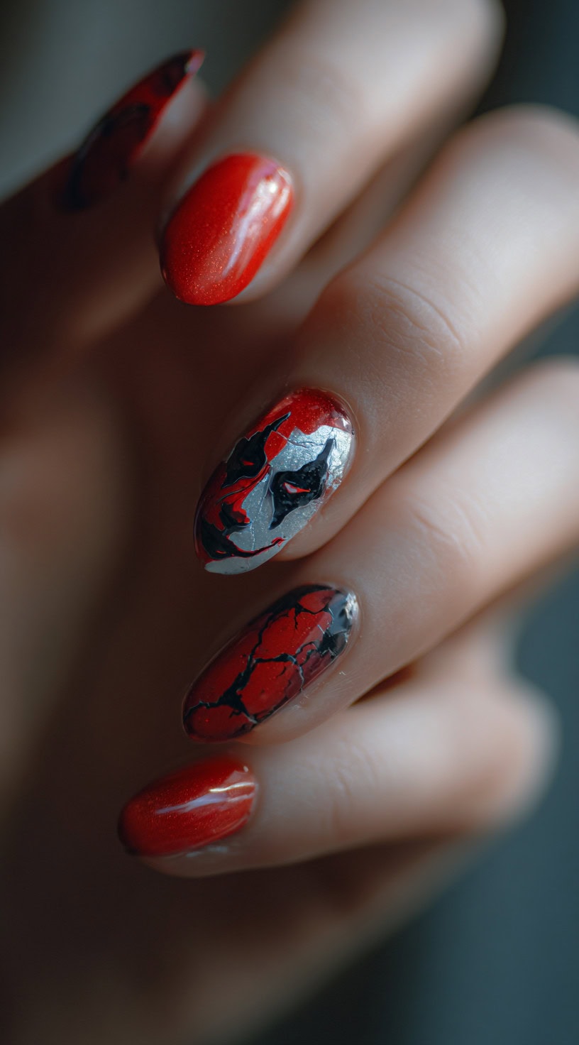 Almond-shaped nails in deep red with a silver Joker face, metallic highlights, and shattered crackle texture accents.