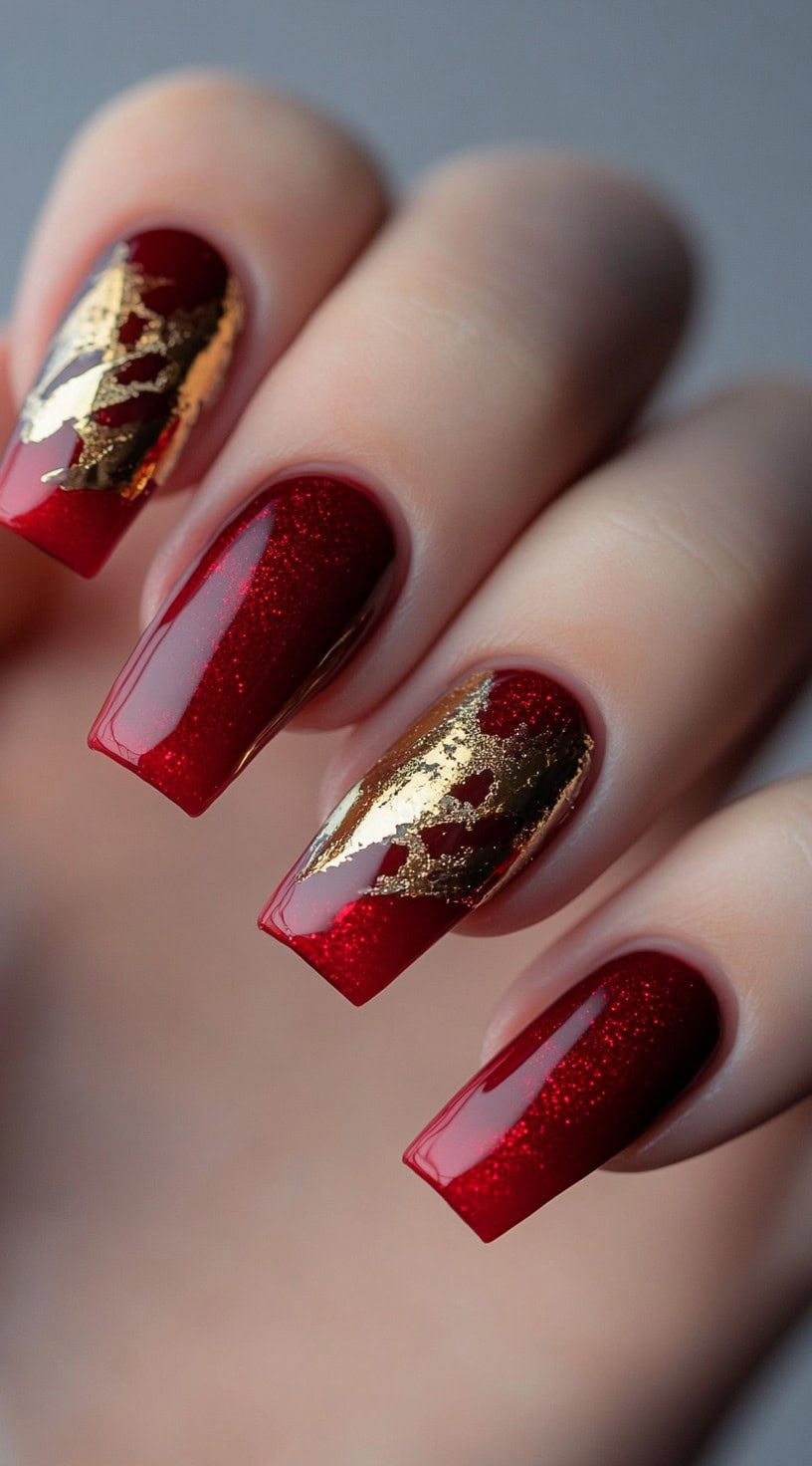 Red glitter nails in a coffin shape featuring artistic gold foil embellishments for a regal finish.