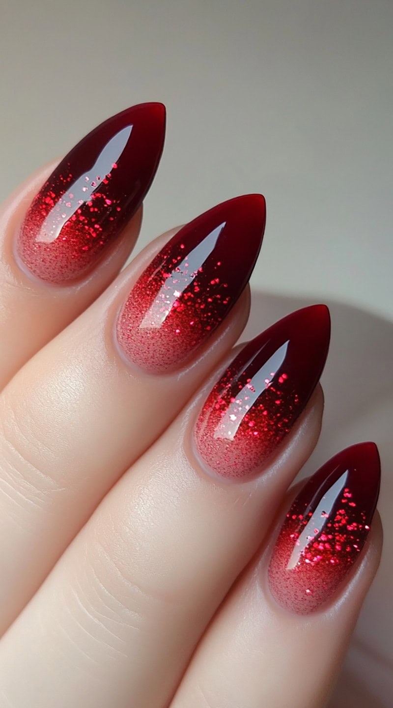 Almond-shaped nails with a gradient red glitter ombre fading from the base to a deep red tip.