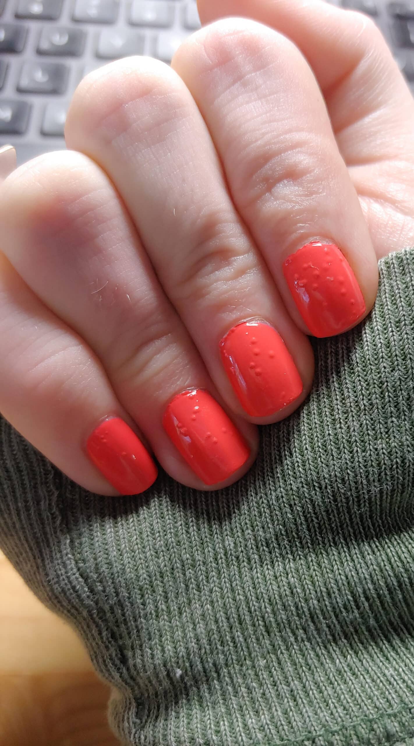 Multiple nails painted in glossy red polish displaying visible tiny bubbles and uneven surface texture across the manicure.