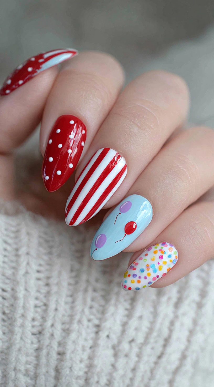 Five almond-shaped nails with alternating red and white dots, stripes, and a tiny balloon face design on a blue base.