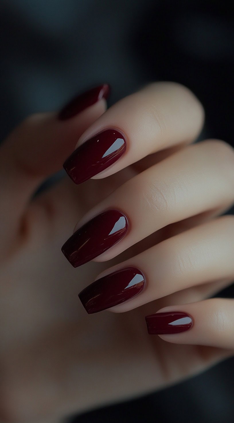 A hand with long square-shaped nails painted in a deep, glossy burgundy shade.
